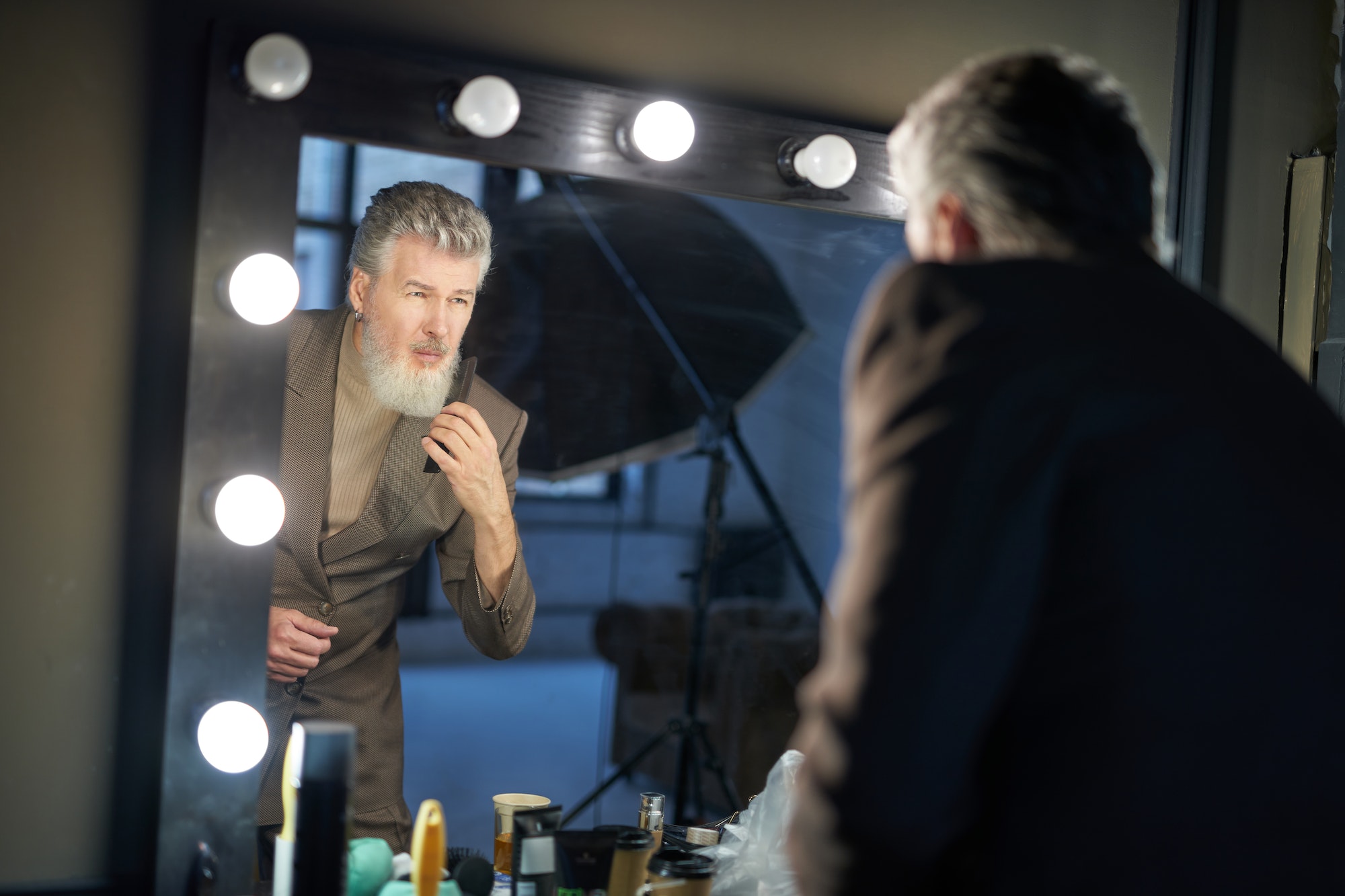 Handsome gray haired middle aged man wearing elegant suit looking at himself in the mirror while