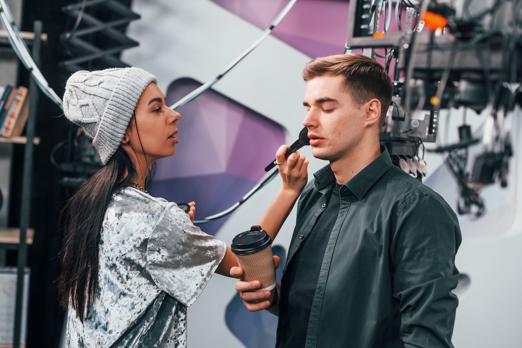 Young man is preparing for TV online broadcast. Woman helps with make up